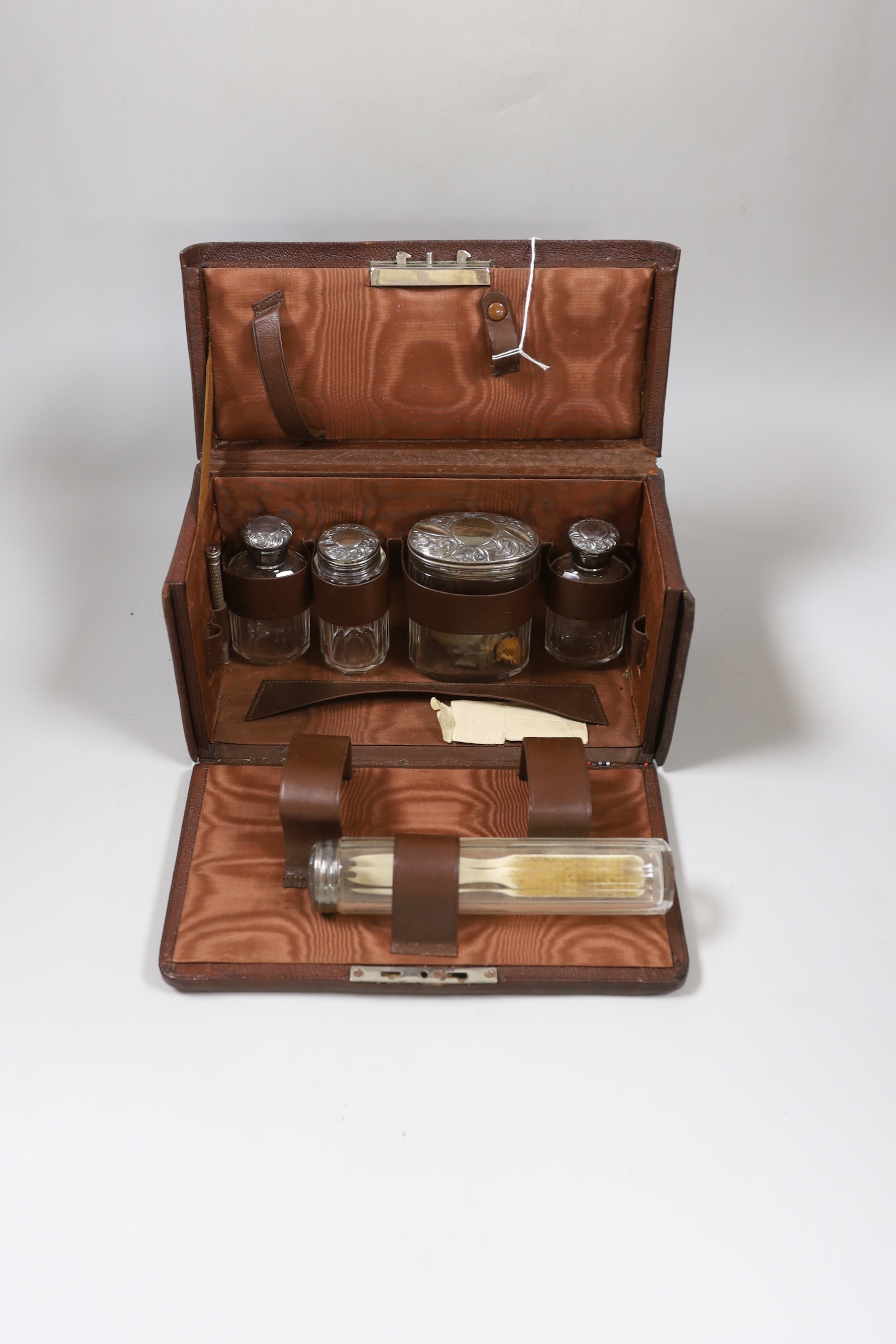 A George V leather travelling toilet case, containing five silver mounted glass jars, Birmingham, 1910, (incomplete), case 25cm.